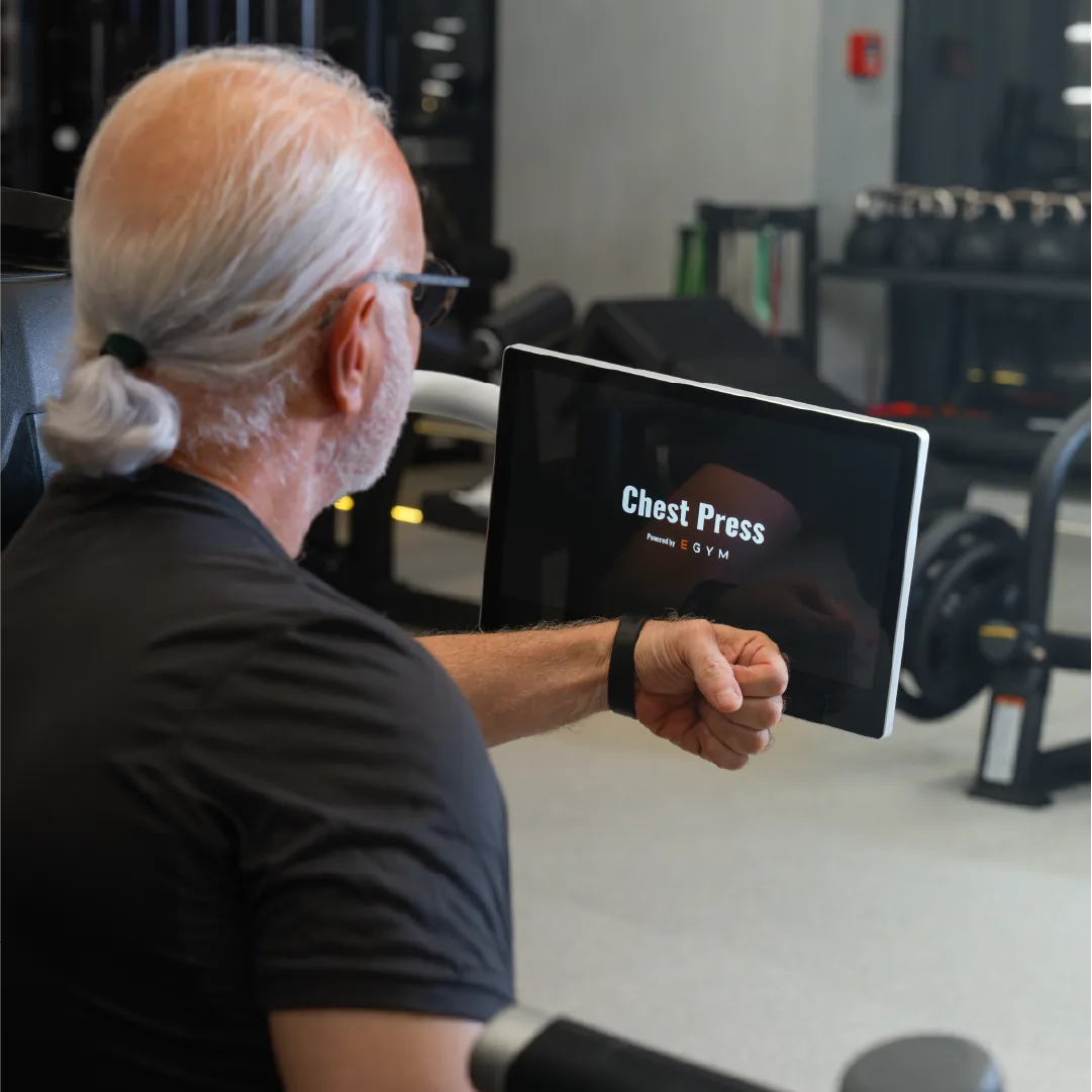 Mitglied startet ein Workout am Trackbar-Display einer Brustpresse