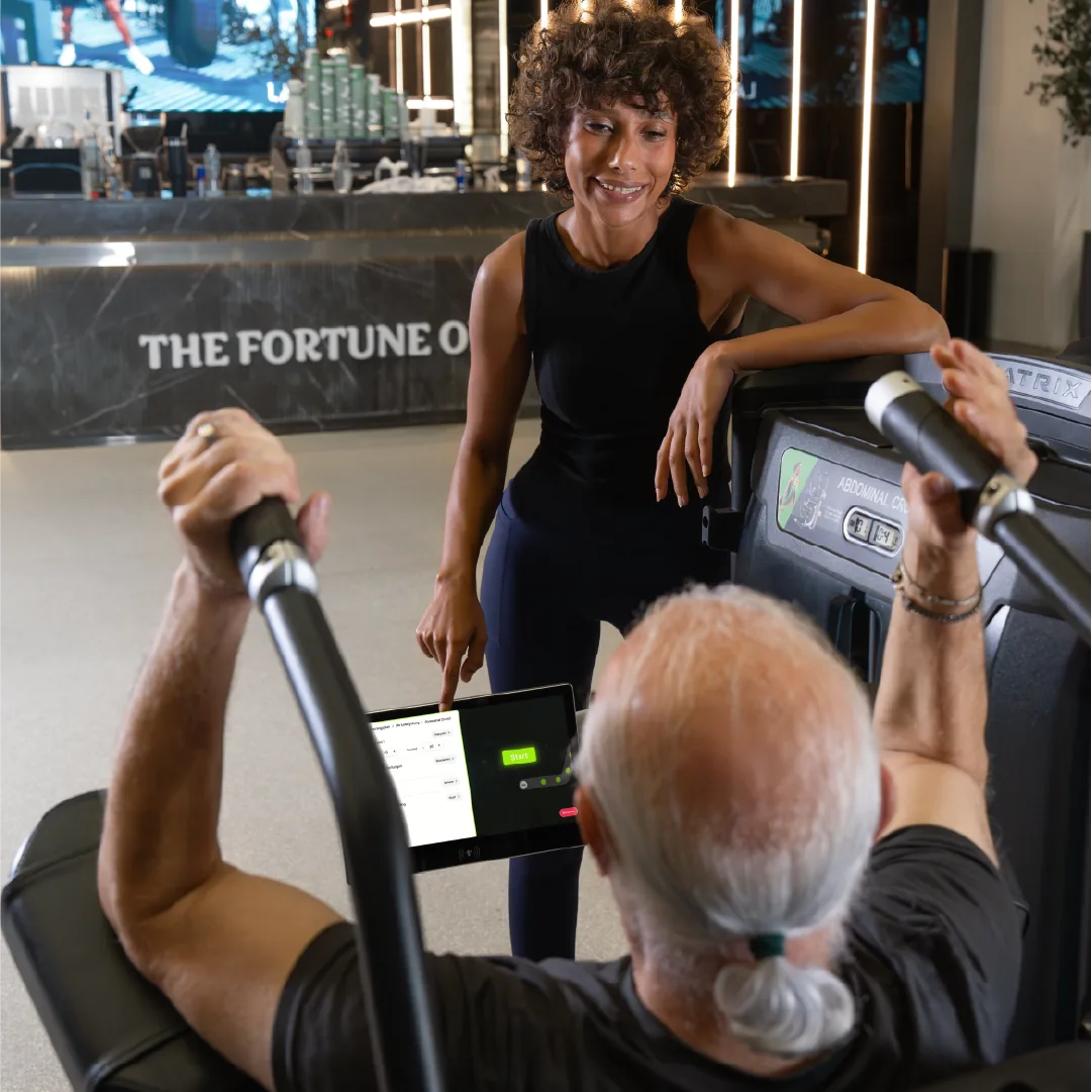 Trainer erklärt einem Mitglied das Trackbar-Display am Kraftgerät